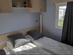 ein Bett mit zwei Kissen und ein Fenster in einem Zimmer in der Unterkunft NORDSEE GLAMPING MobilheimChalet 2154 in Bredene