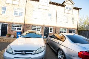 Queens Court Ensuite Studio في ستوك أون ترينت: سيارتان متوقفتان في موقف السيارات أمام مبنى