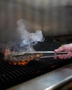 a person cooking a steak on a grill with tongs at Hauser House Unit 1 in Red Lodge