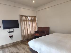 1 dormitorio con 1 cama, 1 silla y TV de pantalla plana en Arara Mhas Hotel, en Cherrapunji