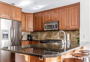 a kitchen with wooden cabinets and a stainless steel refrigerator at Tranquility at Rundle Cliffs Lodge in Canmore