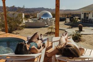 two women laying on chairs next to a swimming pool at Quail Wash Retreat - Star Dome I Sauna I Plunge I Spa in Joshua Tree