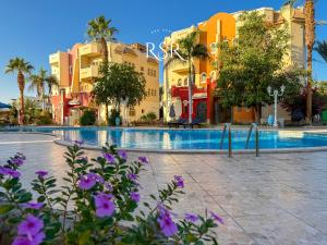 a resort with a swimming pool and palm trees and purple flowers at Green Garden Resort in Hurghada