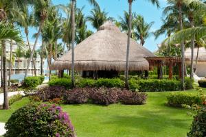 a garden with a thatched pavilion and palm trees at Iberostar Selection Riviera Cancun - All Inclusive in Puerto Morelos