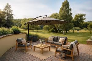 a patio with chairs and a table and an umbrella at Le Hameau des Prés-Verts, un séjour détente et bien être pour les amoureux de la nature au cœur du Pays d'Auge, en Normandie in Les Champeaux