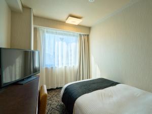 a hotel room with a bed and a flat screen tv at APA Hotel Matsuyamajo Nishi in Matsuyama