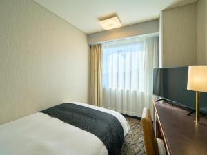 a hotel room with a bed and a flat screen tv at APA Hotel Matsuyamajo Nishi in Matsuyama