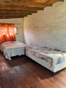 two beds in a room with wooden floors at Cabaña Cica in Punta Del Diablo