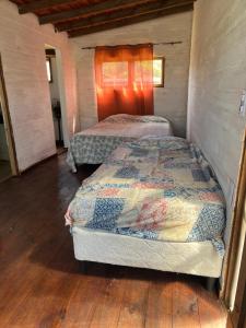 two beds in a room with wooden floors at Cabaña Cica in Punta Del Diablo +2 photos