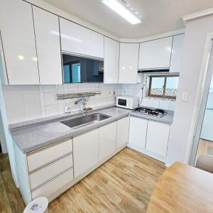 Una cocina con gabinetes blancos y un fregadero y una mesa. en Ocean House PH, en Pohang