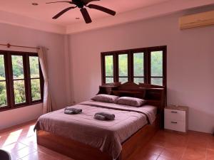 a bedroom with a bed with a ceiling fan and windows at Theorenda house in Ban Taling Ngam