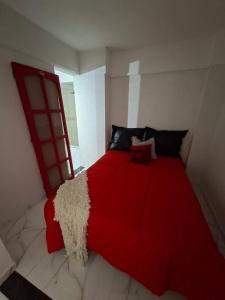 Cama roja en habitación blanca con manta roja en Departamento Vicco, en Pinamar