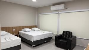 una habitación con 2 camas y una silla negra en Hotel Monte Libano, en Paranaguá