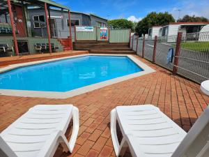 a swimming pool with two white lounge chairs next to it at Warrnambool Motel and Holiday Park in Warrnambool