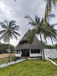 a house with a thatched roof and two palm trees at Artistic Dreamsace 4Br Villa Near Diani Beach in Kwale