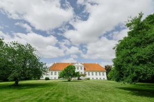 UllerslevにあるManor With Soul Between Forest And Lake On Funenの緑の野原にオレンジ色の屋根が付いた大きな白い建物