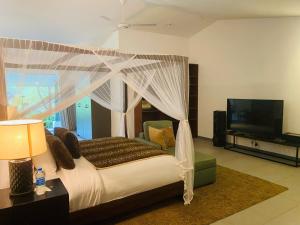 Un dormitorio con una cama con dosel y un televisor de pantalla plana. en Rain Drops Wellness Villa Sinharaja, en Mederipitiya