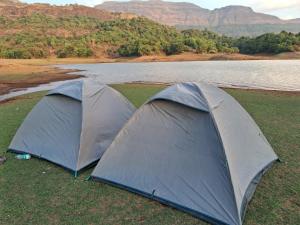 班达尔达拉Bhandardara I land Camping的水体旁的草地上搭着两顶帐篷。