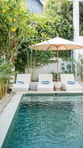 a swimming pool with two chairs and an umbrella at The White Bay Lombok in Kuta Lombok