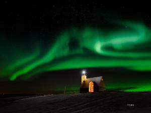 uma aurora sobre um celeiro com uma torre num campo em Úthlíd Cottages em Úthlid