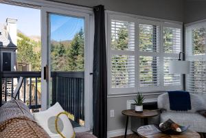 ein Wohnzimmer mit einem Sofa und einem Balkon mit Fenstern in der Unterkunft Stay A While Ski-In-Out Hot Tub & Shuttle in Blue Mountains