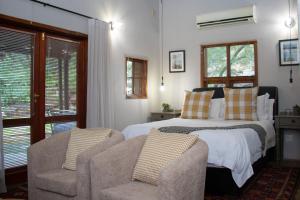 比勒陀利亚舍伍德小屋酒店的一间卧室，里面有一张床、一把椅子和几扇窗户。