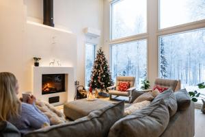 a woman sitting on a couch in a living room with a christmas tree at Villa Lumossa - Lakeside Luxury with unique privacy in Rovaniemi