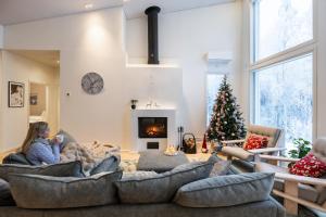a woman sitting on a couch in a living room with a christmas tree at Villa Lumossa - Lakeside Luxury with unique privacy in Rovaniemi