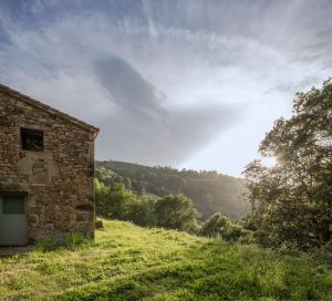 a stone building on a grassy hill with the sun in the sky at Casa Mínima retiro Passivhaus in Selaya +29 photos