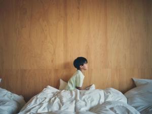 a little boy sitting on top of a bed at SANU 2nd Home Ichinomiya 2nd in Ichinomiya