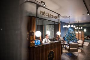 a man sitting at a reception desk with a christmas tree at Hotel D Bulle - La Gruyère in Bulle
