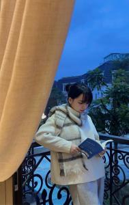 a woman standing on a balcony reading a book at Huế Nestory Homestay in Thôn Trường Giang