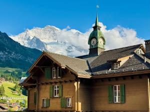 un edificio con una torre de reloj con montañas al fondo en Eiger Residence 3, en Wengen