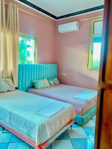 Dos camas en una habitación con paredes y ventanas rosas. en Hotel Complex Europe, en Guercif