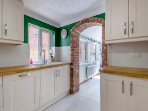 a kitchen with white cabinets and a brick wall at Ravensmere Villa in Beccles