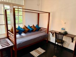 a bedroom with a bed with blue pillows and a desk at The Colony Hotel in Habaraduwa