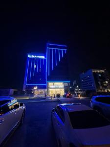 阿布扎比Saray Deluxe Hotel Apartments的夜晚，一栋蓝色建筑的停车场里停满了汽车。