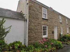 een oud stenen huis met bloemen ervoor bij 1 Rowes Cottages in Porthcurno