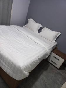 een bed met witte lakens en kussens erop bij The Home Apartments in Kolwezi