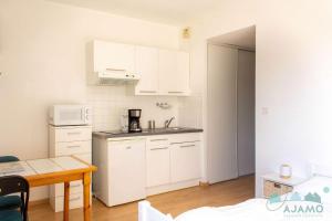 una pequeña cocina con armarios blancos y una mesa en 104 - Studio, dans une résidence les pieds dans l'eau à Sables D'or Les Pins, en Sables-dʼOr-les-Pins