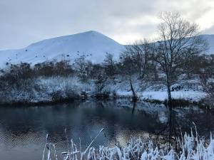 a snow covered mountain next to a body of water at Maggie's Barn in Talgarth