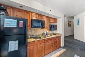 a kitchen with wooden cabinets and a black refrigerator at Beach Cove Resort - Oceanfront Condo - Unit 1516 in Myrtle Beach