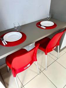ジョアンペソアにあるMelhores Flats - Maravilhosa varanda frente ao marのテーブル(赤い椅子、白い皿、グラス付)