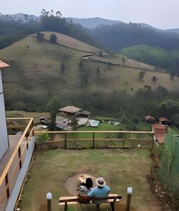 two people sitting on a bench looking at a mountain at Recanto dos Canários - CHALÉ 1 in Visconde De Maua