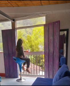 una donna seduta su un balcone che guarda fuori da una finestra di Hostal Casa Pijao a Pijao