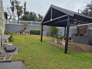 a pavilion in a yard with benches and a fence at Jakaranda Holiday Flat in Uvongo Beach