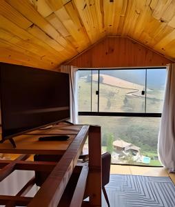 a large window in a room with a desk with a television at Recanto dos Canários - CHALÉ 1 in Visconde De Maua +31 photos