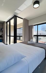 a bedroom with a large white bed and large windows at Studio Compacto com Design Clean no Vertigo in Campo Grande +23 photos