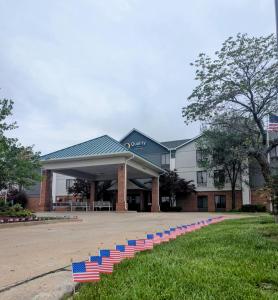 Quality Inn Warrensburg في ارنسبورغ: مبنى عليه أعلام حمراء وبيضاء وزرقاء على العشب