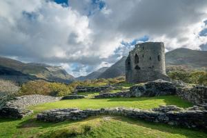 an old building on a field with mountains in the background at Adwyr-Mynydd in Dinorwic